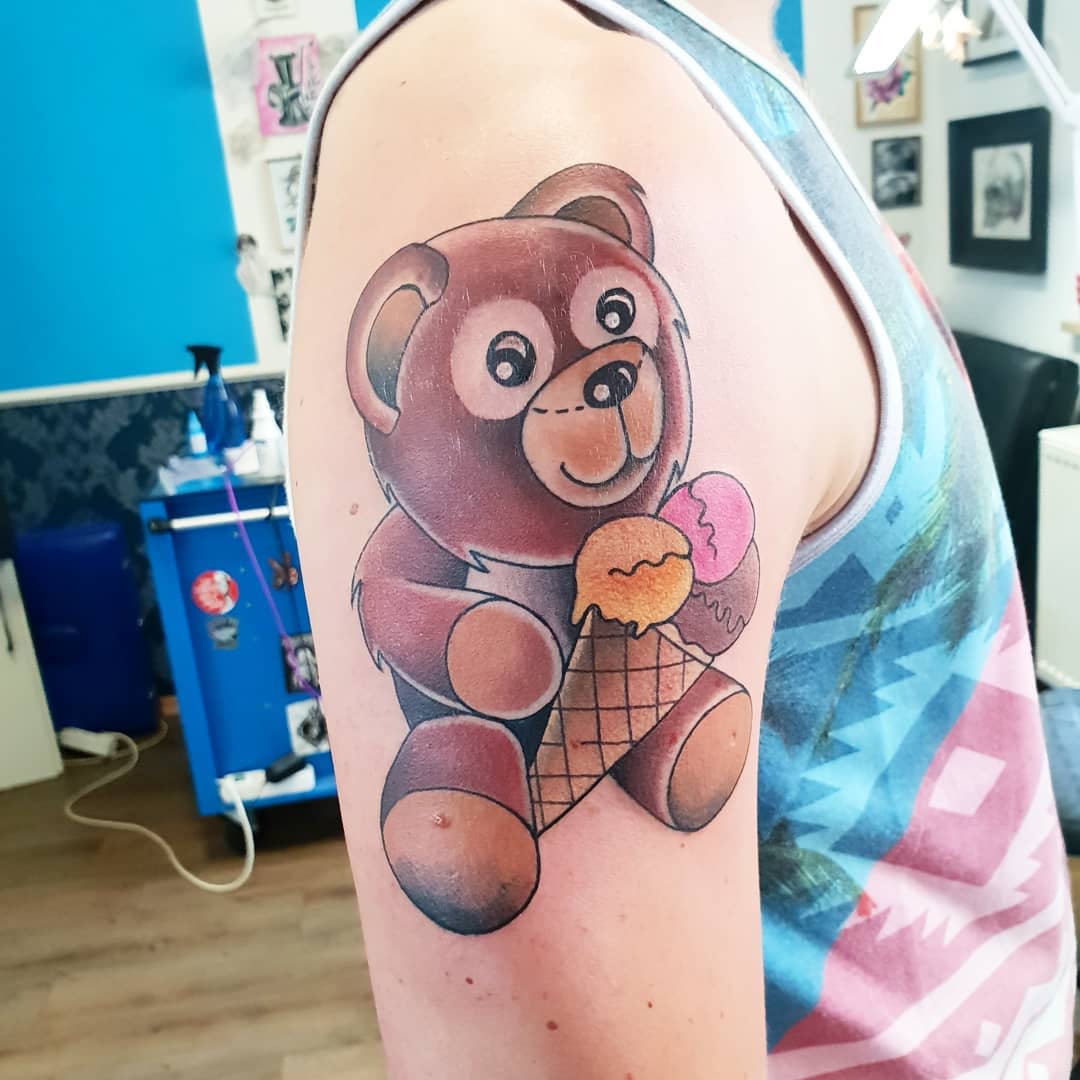 Tattoo of a teddy bear holding an ice cream cone on someone's upper arm